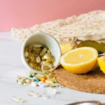 witaminy w tabletkach rozsypane na stole, obok położona jest cytryna i imbir