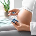Kobieta w ciąży trzyma w ręku suplementy diety w kapsułkach